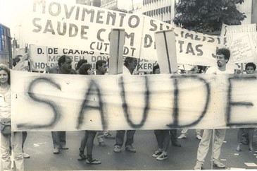 Imagem preta e branca da manifestação de pessoas com cartazes demandando qualidade em saúde