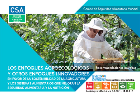 Galpão rústico com pessoas sentadas no chão em roda e uma pessoa em pé falando.