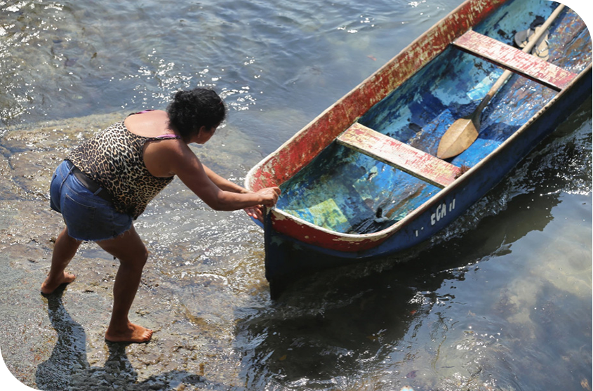 Mulher empurrando uma jangada na beira de um rio. 