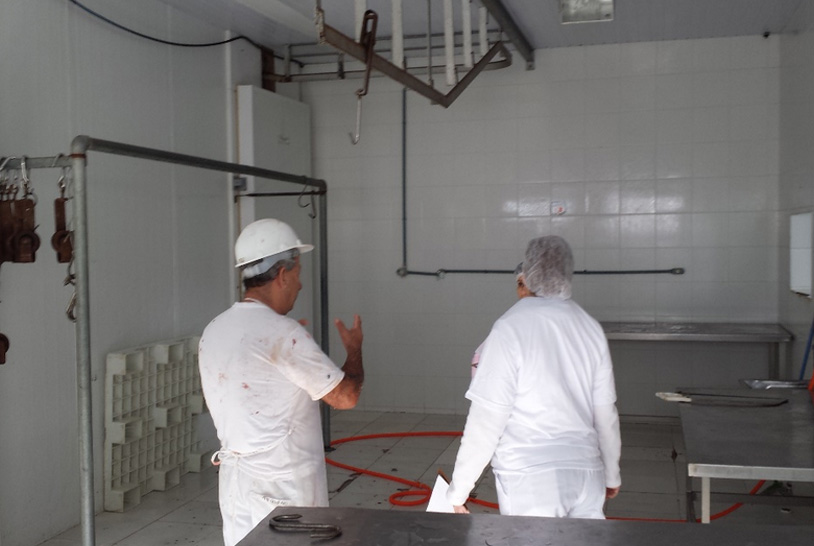Dois trabalhadores uniformizados conversando em uma sala de um frigorífico.